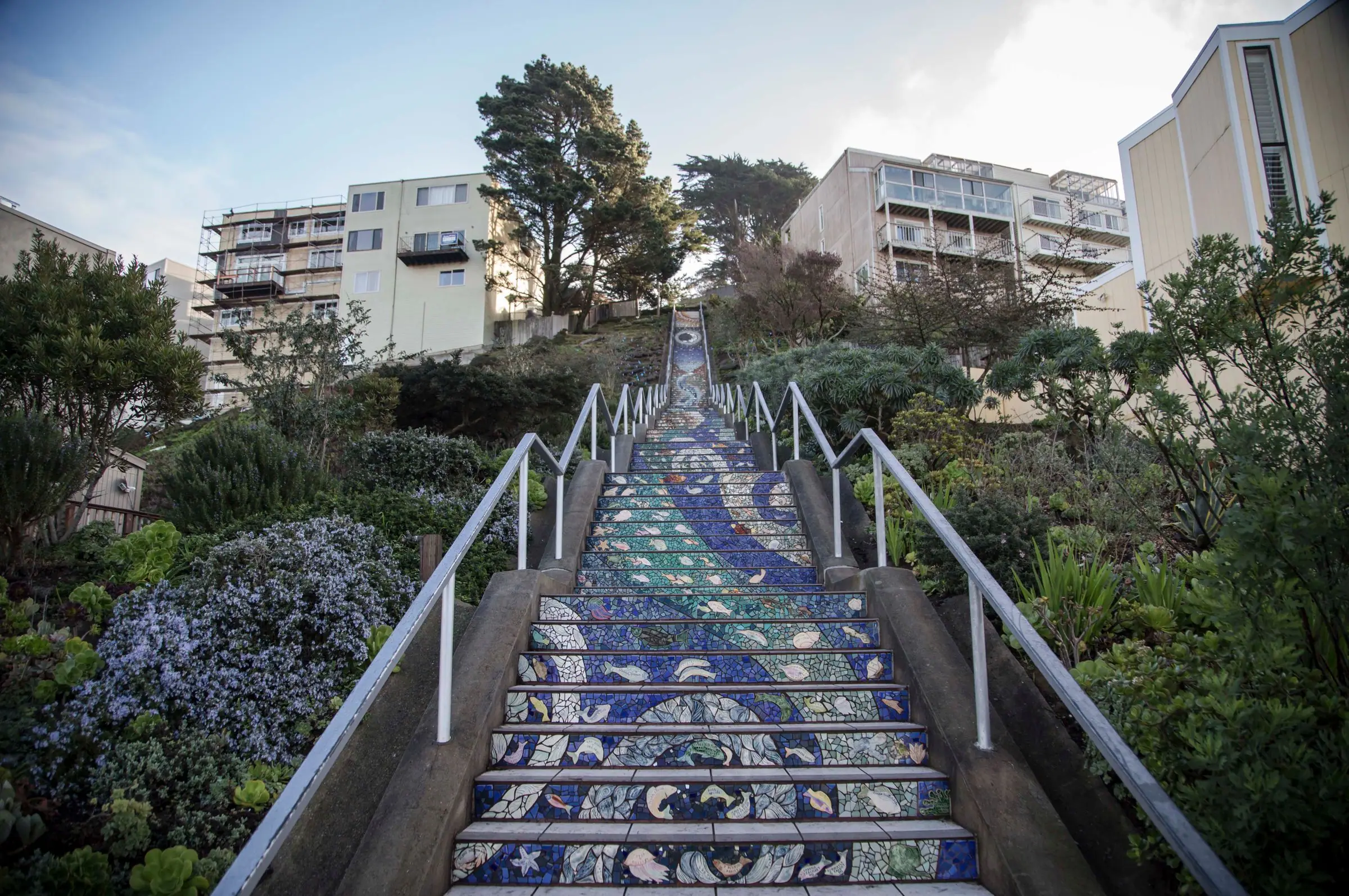 A mosaic-tiled public stairway climbing between gardens and homes