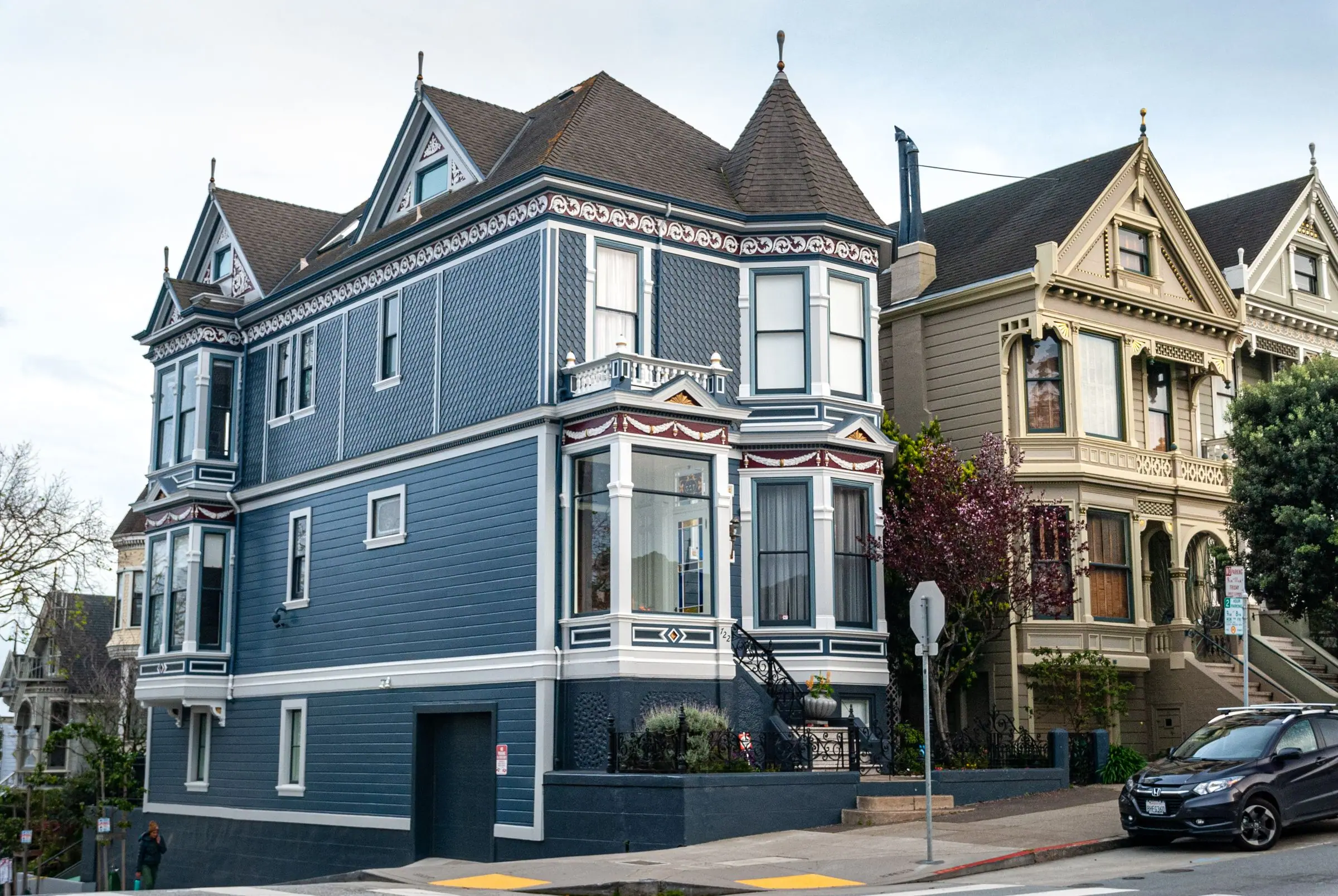 A slate-blue Queen Anne Victorian on a street corner next to a cream Victorian