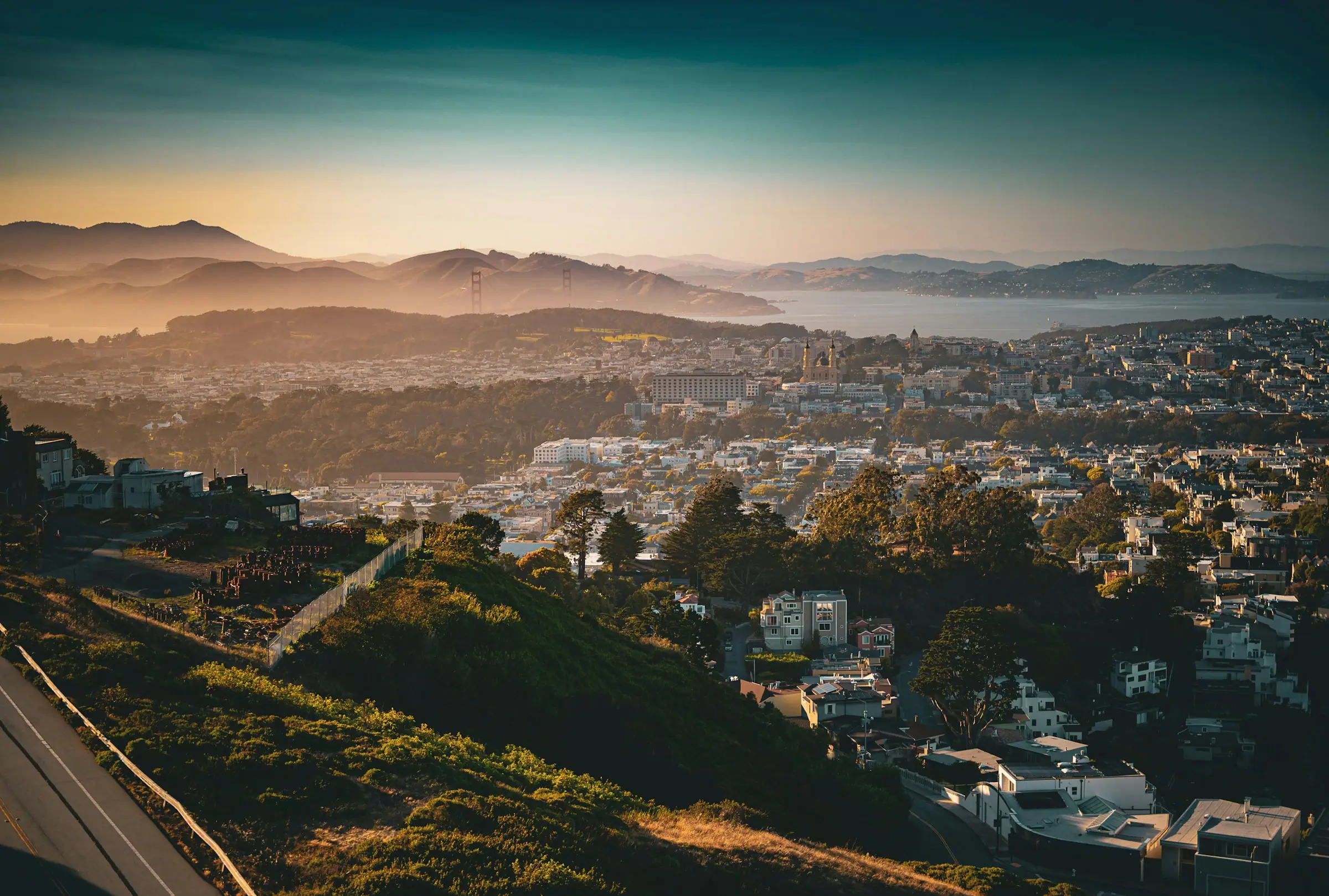 Golden-hour view from Twin Peaks over hillside homes toward the Golden Gate Bridge and the Marin hills