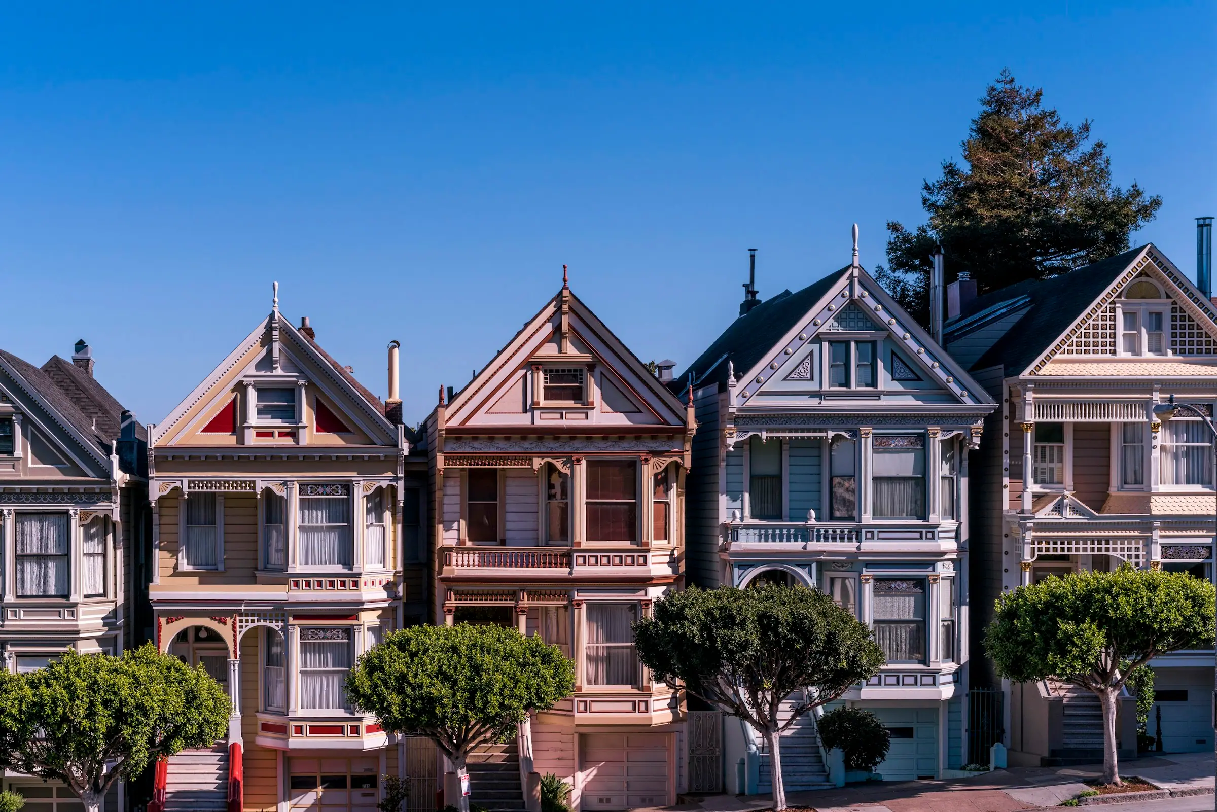 A row of Queen Anne Victorian houses with pointed gables and bay windows under a blue sky